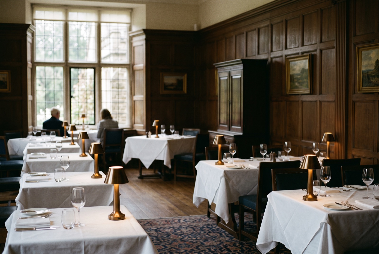 A wood-panelled dining room with white tablecloths and brass lamps