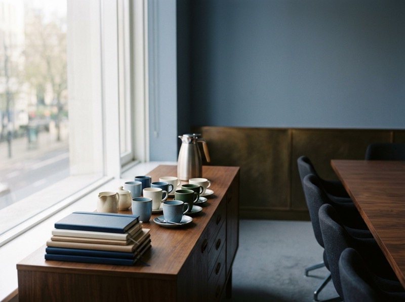 A boardroom sideboard with coffee cups and a stack of closed notebooks, morning light