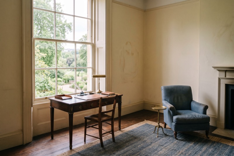 A drawing room with a writing desk and a view of a park