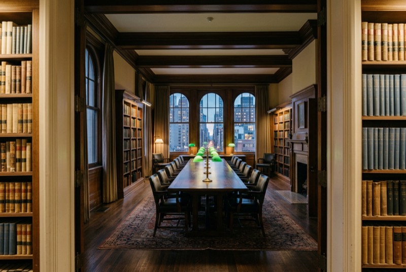 A club library with green reading lamps and a long table