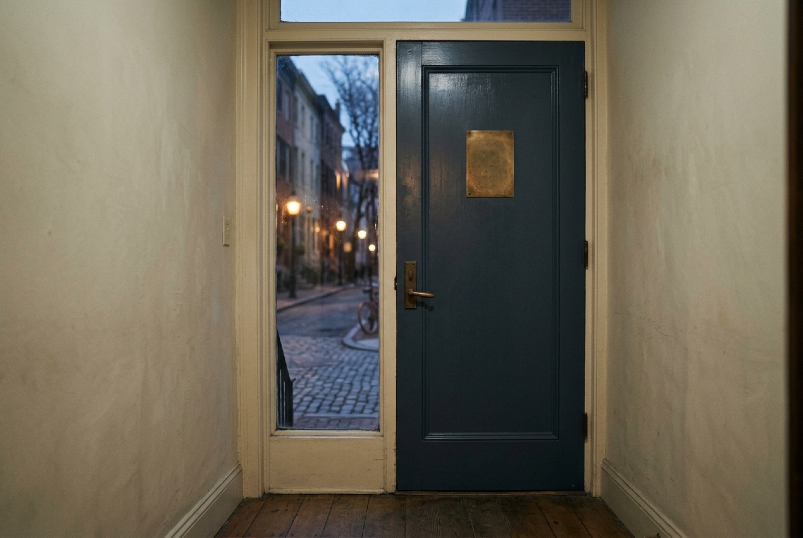 An unmarked townhouse door with a blank brass plate on a quiet street